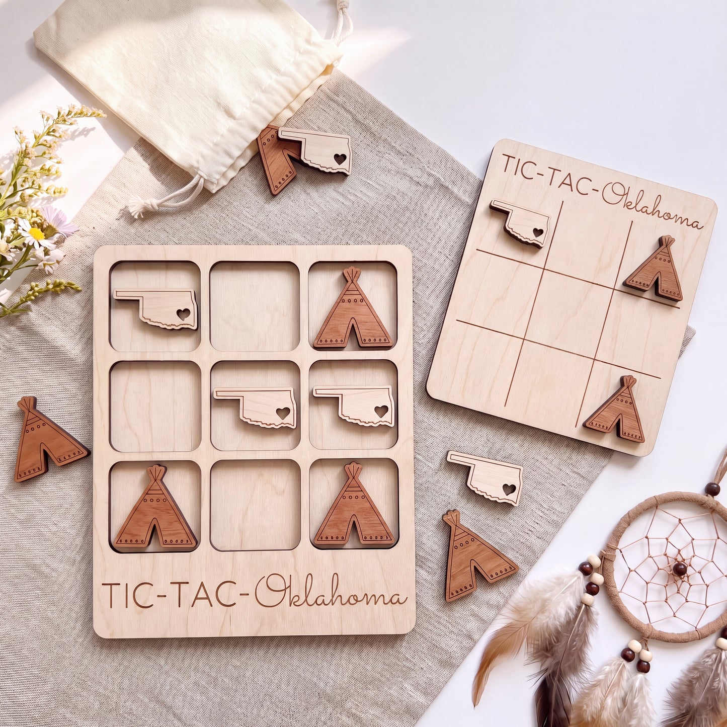 a wooden tic-tac game set with wooden pieces shaped like the state of Oklahoma, along with a dreamcatcher and some flowers.