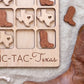 a wooden game board with a Texas state map cut out, along with wooden boot cutouts, and a pair of brown leather boots.