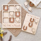 a wooden tic-tac game set with wooden pieces shaped like horseshoes, labeled "TIC-TAC-Nebraska". The game is placed on a beige cloth, and there are some additional wooden pieces scattered around the game.