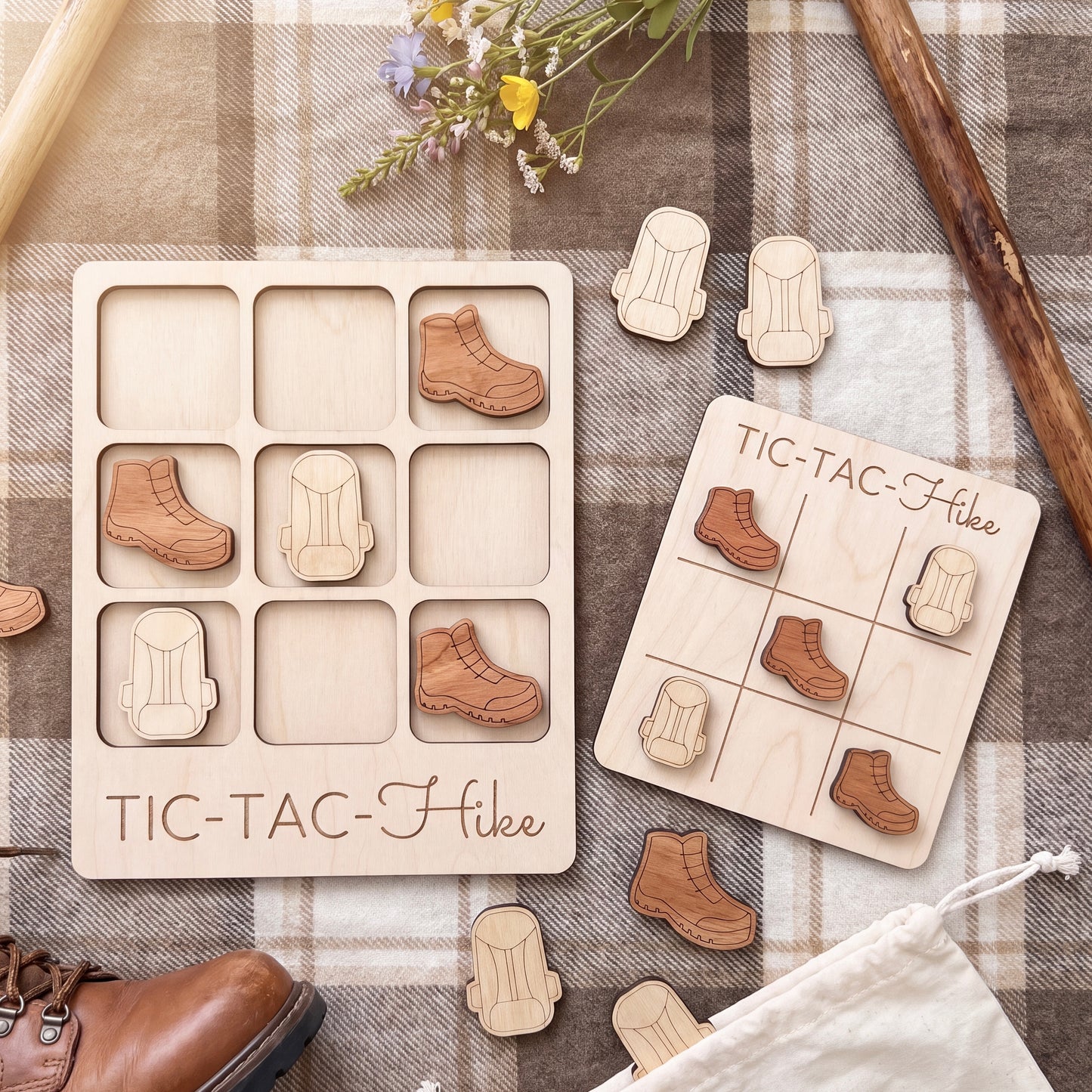 a wooden tic-tac-toe game with wooden pieces shaped like hiking boots, placed on a plaid cloth. There are also some wooden objects, such as a pair of boots, scattered around the game.