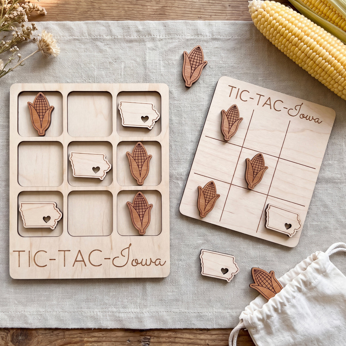 a wooden game board labeled "TIC-TAC-IOWA" and a set of wooden game pieces with cornucopia designs, all placed on a wooden surface.