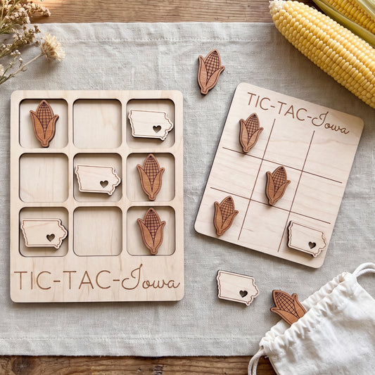 a wooden game board labeled "TIC-TAC-IOWA" and a set of wooden game pieces with cornucopia designs, all placed on a wooden surface.
