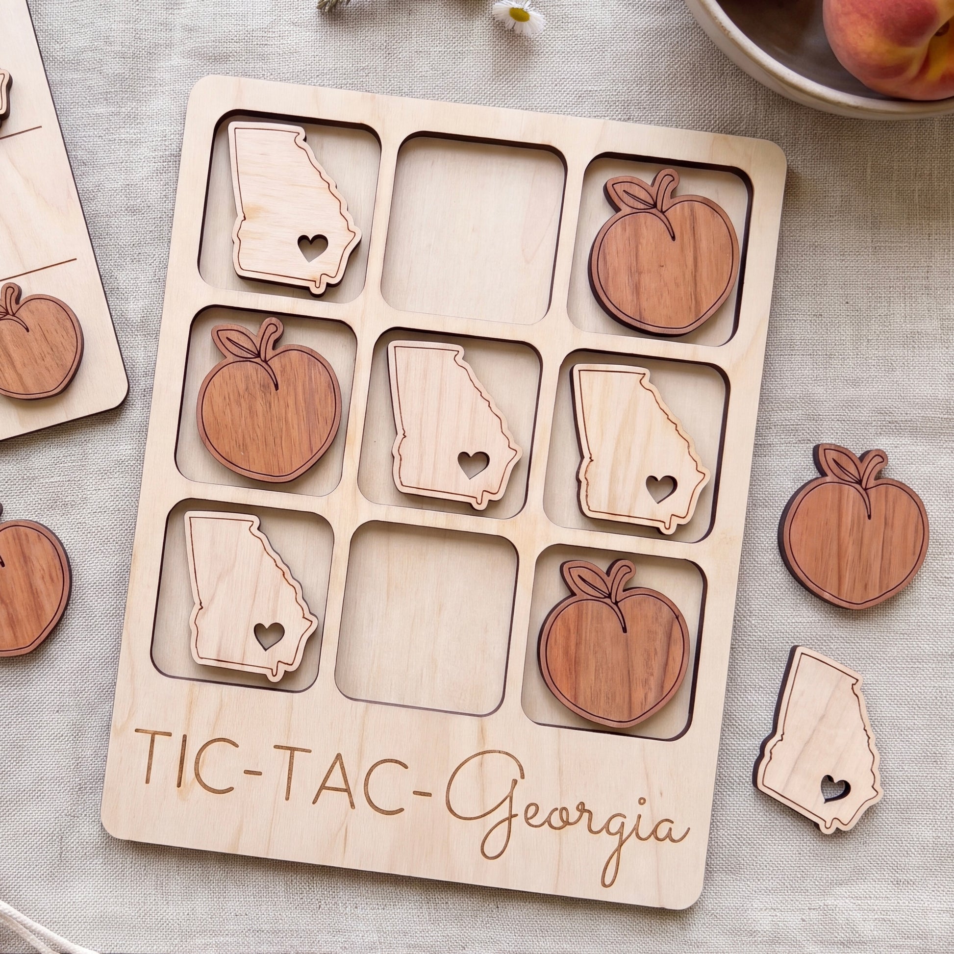 A wooden tic-tac game board with wooden pieces shaped like states and apples, labeled "TIC-TAC-Georgia".
