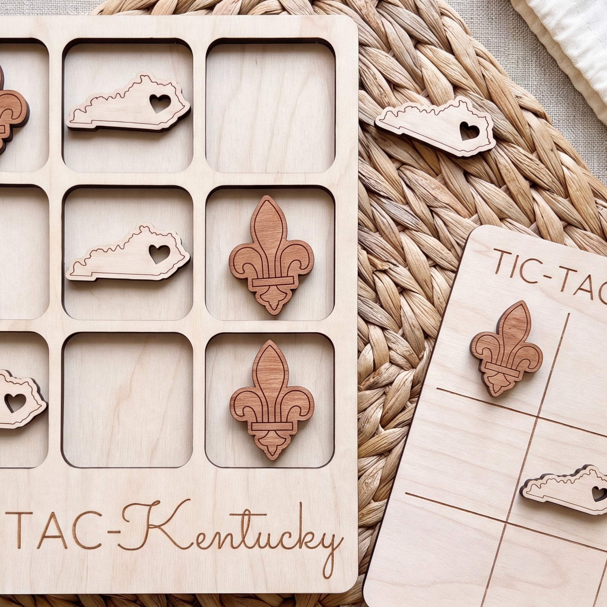 a wooden game board with a tic-tac game board and wooden pieces shaped like hearts and fleur-de-lis, all labeled with the word "TAC-KENTUCKY".