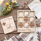 a wooden tic-tac game set with wooden pieces shaped like states in New Mexico, along with a wooden card that reads "TIC-TAC New Mexico". The game pieces are placed on a wooden surface, and there are some flowers and a white cloth in the background.