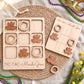 a wooden tic-tac game set with Mardi Gras beads and masks, arranged on a woven placemat.