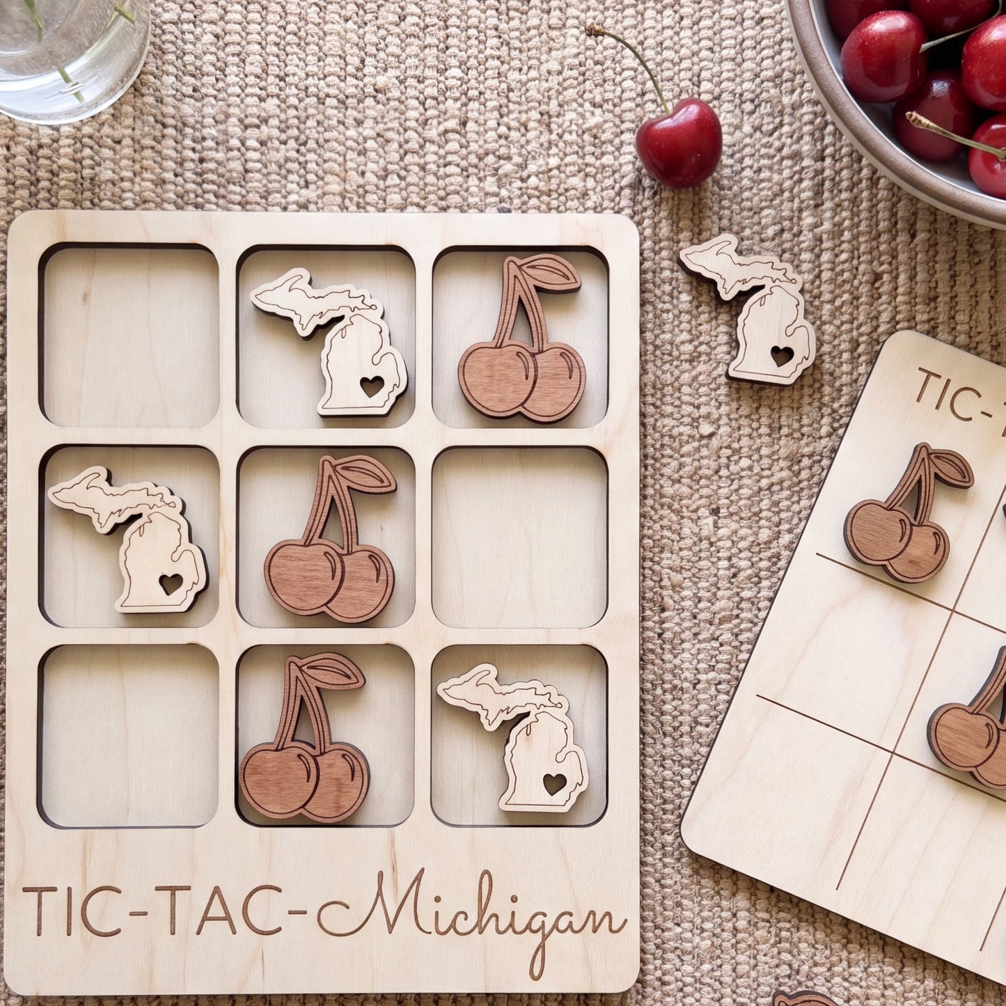 a wooden tic-tac game board with a Michigan theme, including wooden cherries and a bowl of cherries. The board is labeled "TIC-TAC-Michigan".