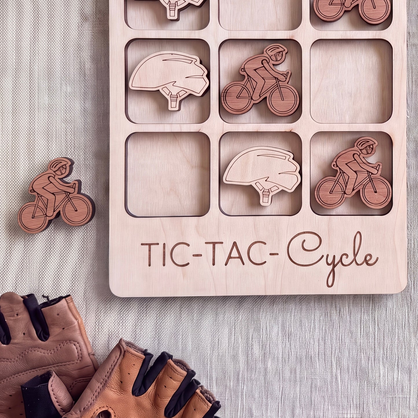 a wooden tic-tac-cycle game board with wooden pieces shaped like bicycles and helmets, along with a pair of leather gloves.
