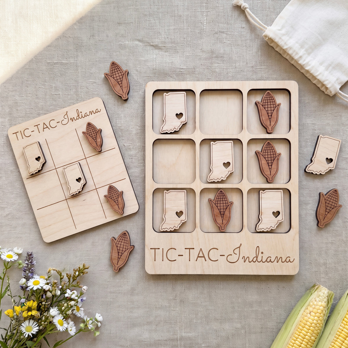 a wooden tic-tac game with Indiana state stickers, a white cloth, and some flowers.