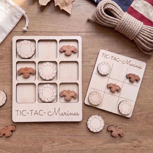 a wooden tic-tac game set with wooden pieces shaped like birds, specifically "Marines", arranged on a wooden surface. There is also a rope and some leaves in the background.