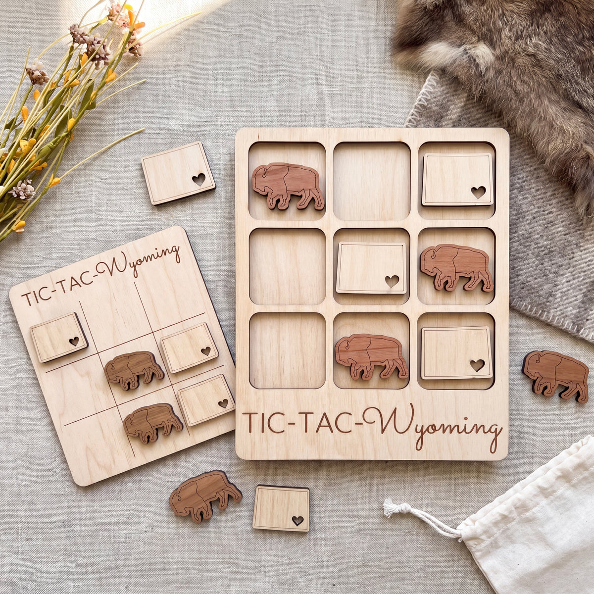 a wooden tic-tac game set with wooden pieces shaped like buffalo, placed on a grey surface.
