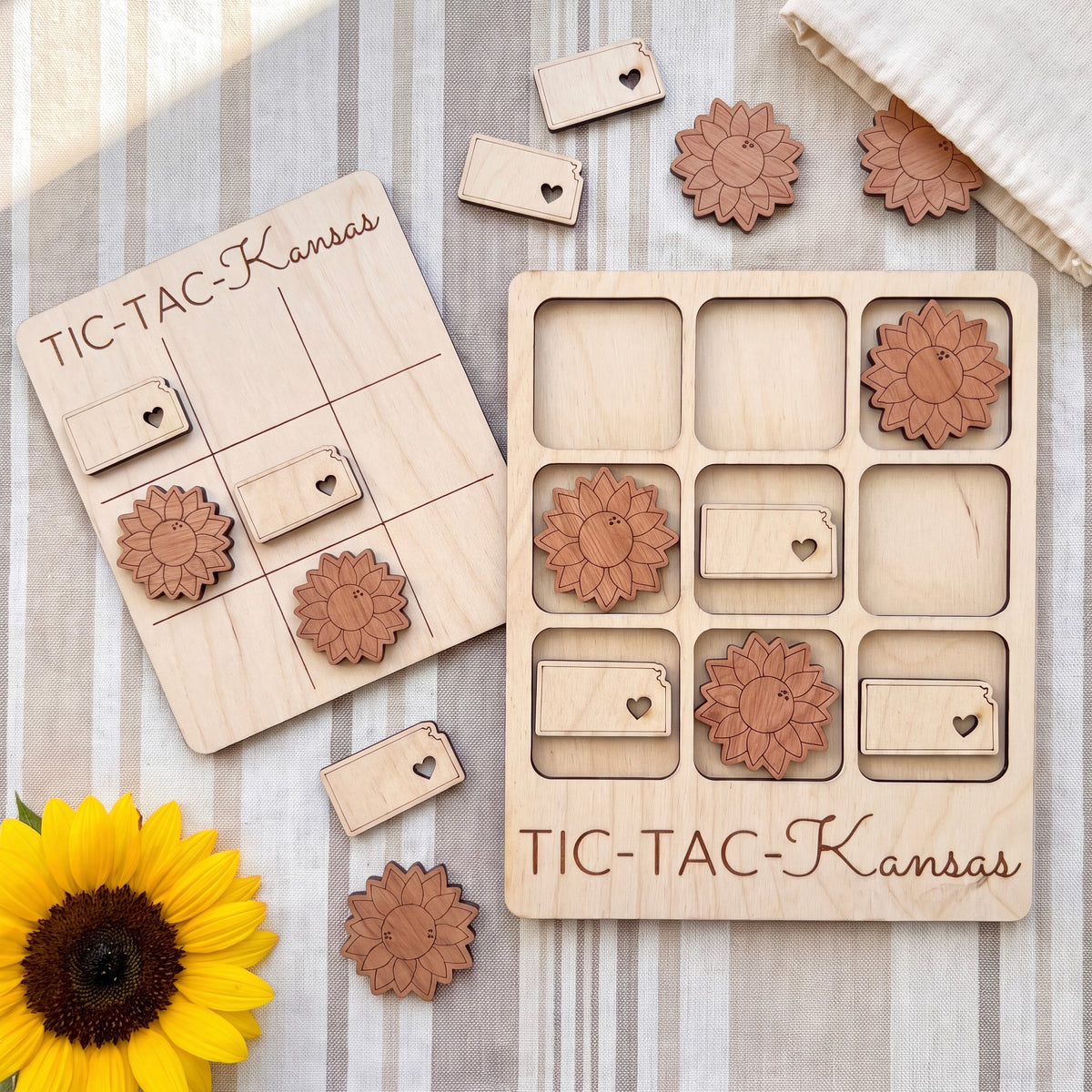 a wooden Tic-Tac- Kansas game board with wooden pieces and a yellow sunflower on a striped surface.