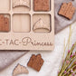 a wooden tic-tac game with wooden crowns on it, along with some pink flowers and a gray cloth.
