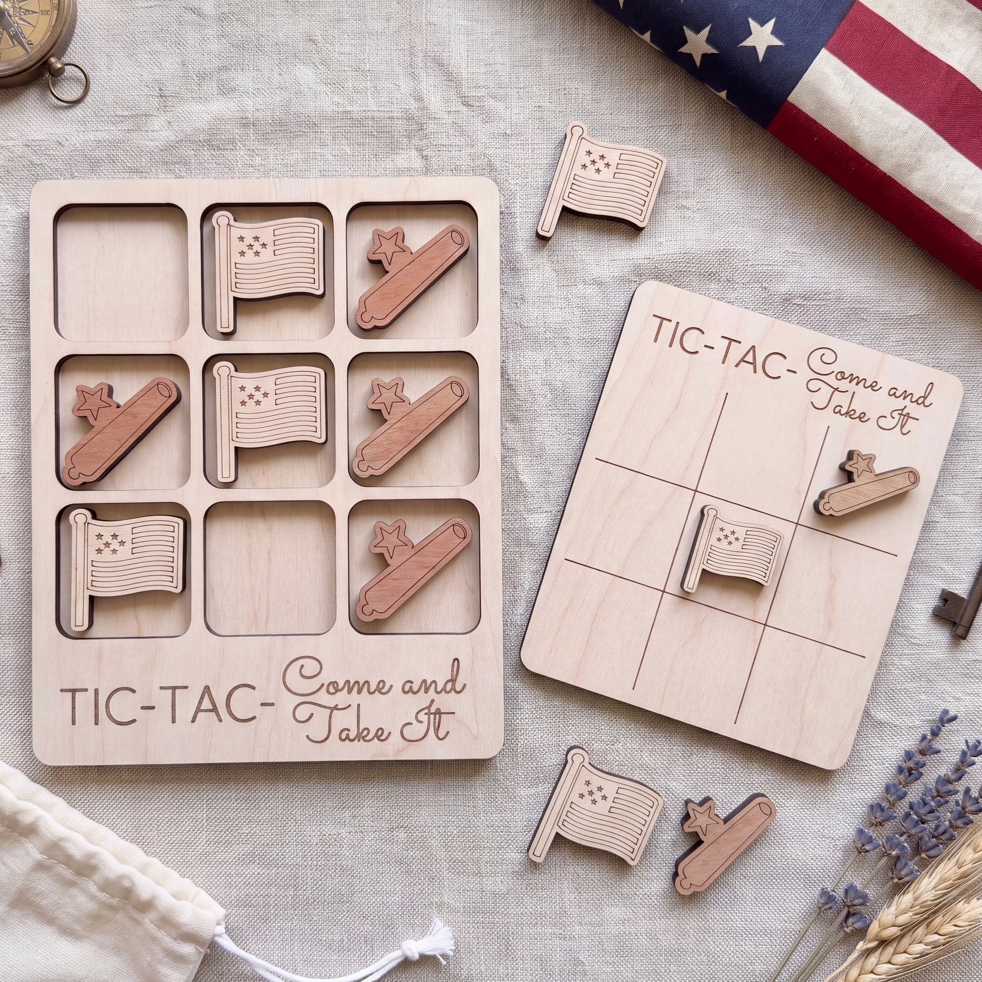 a wooden tic-tac game with a patriotic theme, including an American flag and a tic-tac board with the phrase "TIC-TAC-Come and Take It". The game pieces are also visible, along with a compass and some flowers.