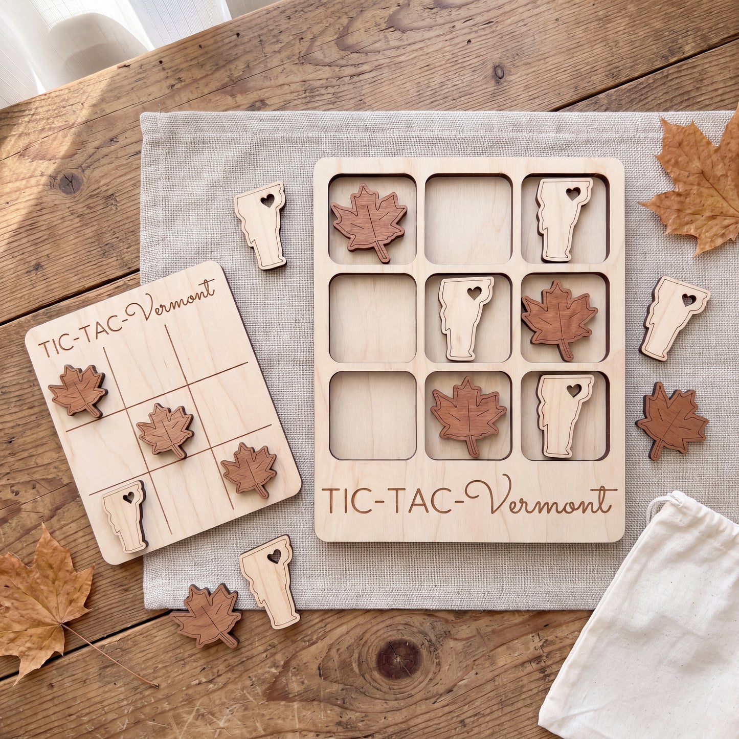a wooden tic-tac game with Vermont-themed pieces, including a game board and pieces, as well as some autumn leaves scattered around the table.
