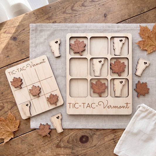 a wooden tic-tac game with Vermont-themed pieces, including a game board and pieces, as well as some autumn leaves scattered around the table.