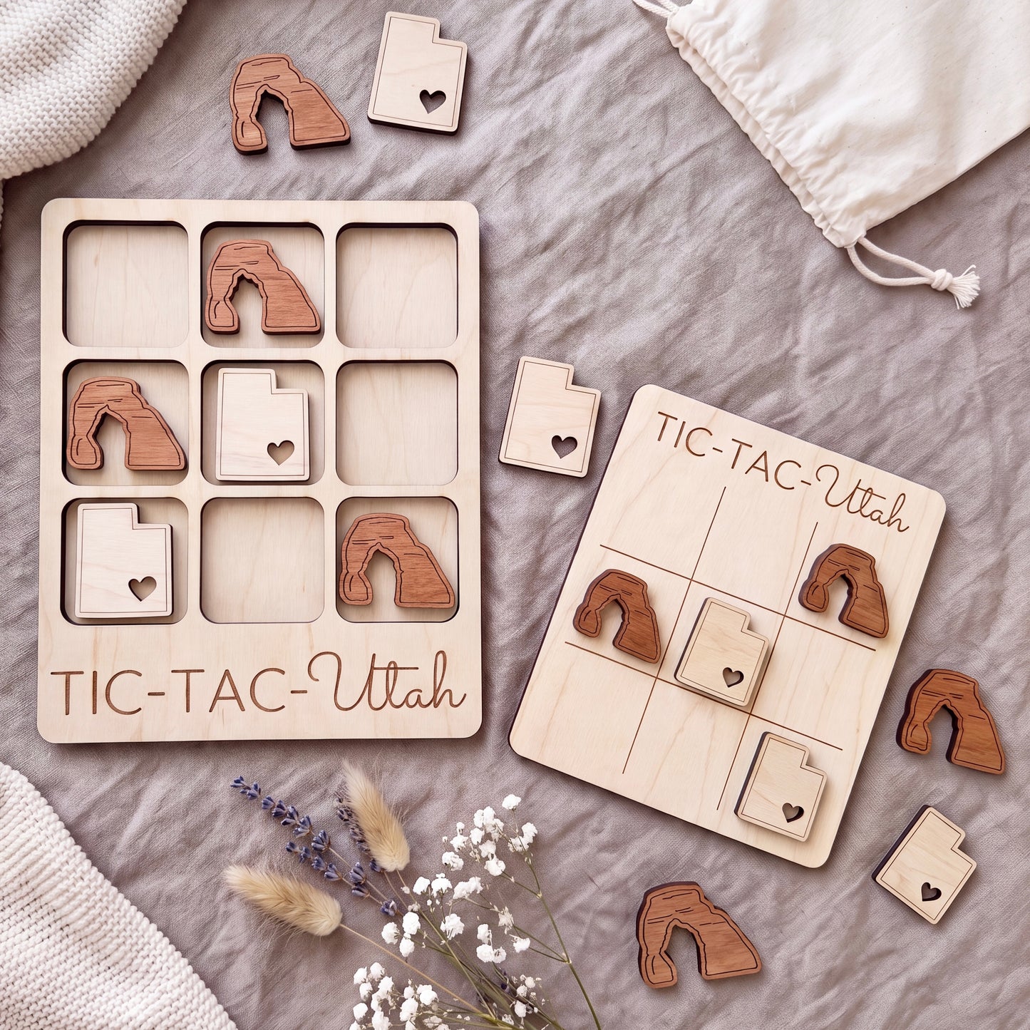 a wooden tic-tac game set with wooden pieces shaped like Utah state icons, placed on a grey surface alongside some flowers.