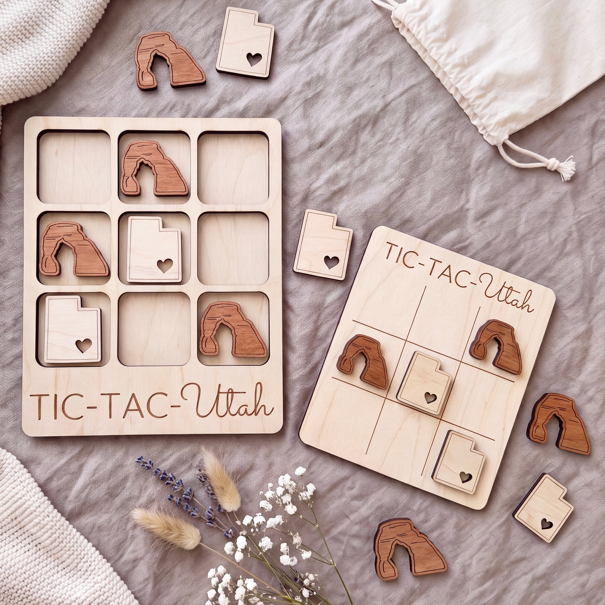 a wooden tic-tac game set with wooden pieces shaped like Utah state icons, placed on a grey surface alongside some flowers.