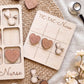 a wooden tic-tac game board labeled "TIC-TAC-NURSE" and various wooden heart-shaped game pieces, including a stethoscope, scattered on a woven surface.