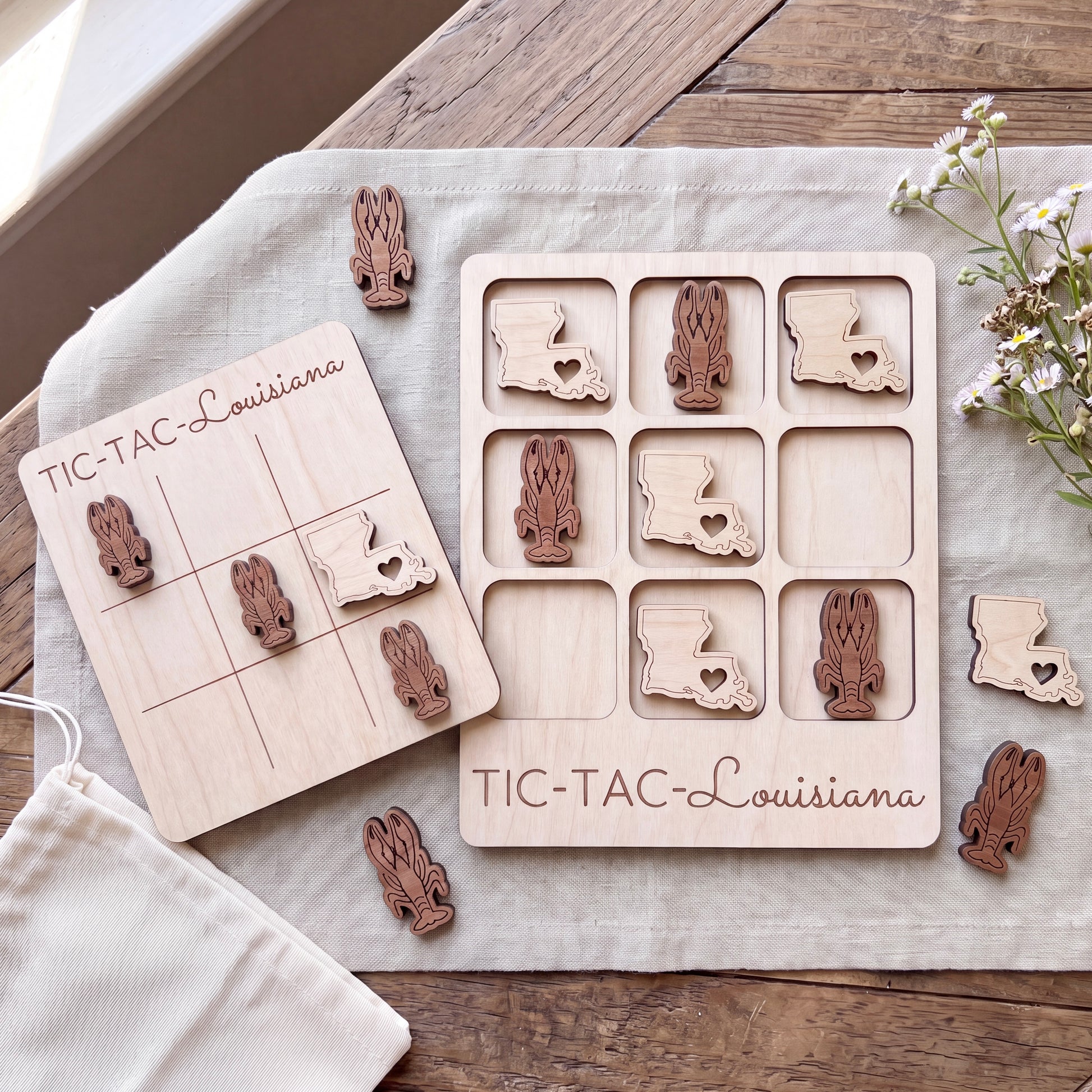 a wooden game board and wooden pieces shaped like rabbits, with the word "TIC-TAC-Louisiana" written on them. The game board and pieces are placed on a wooden surface, surrounded by some flowers.