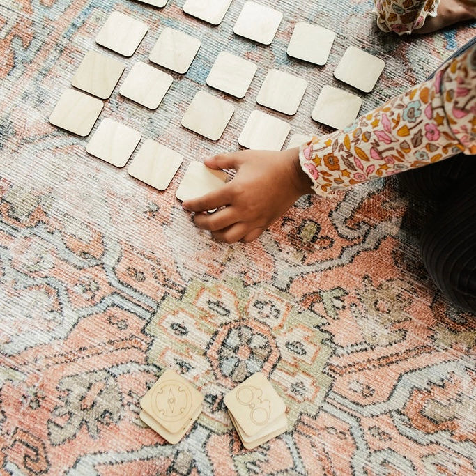 A person's hand is reaching for a small wooden block on a patterned rug.