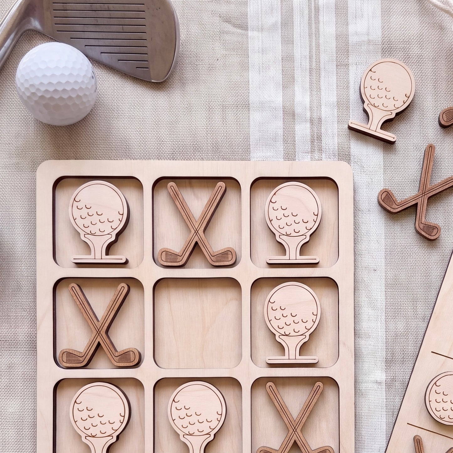 a wooden tic-tac-toe game with golf balls and clubs as the game pieces, arranged on a table with a golf club and ball nearby.