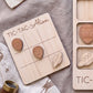 a wooden tic-tac game board with wooden alien and spaceship tiles, along with a wooden tic-tac game piece.