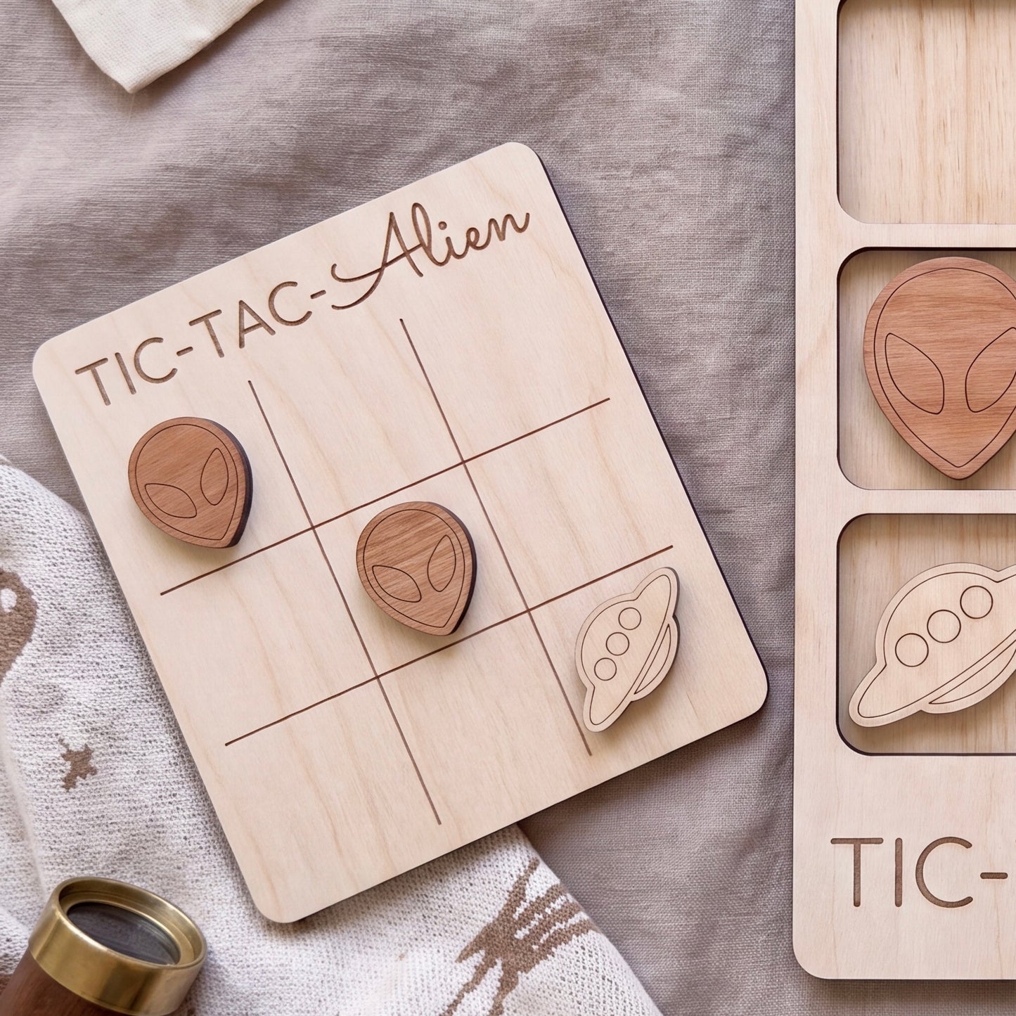 a wooden tic-tac game board with wooden alien and spaceship tiles, along with a wooden tic-tac game piece.