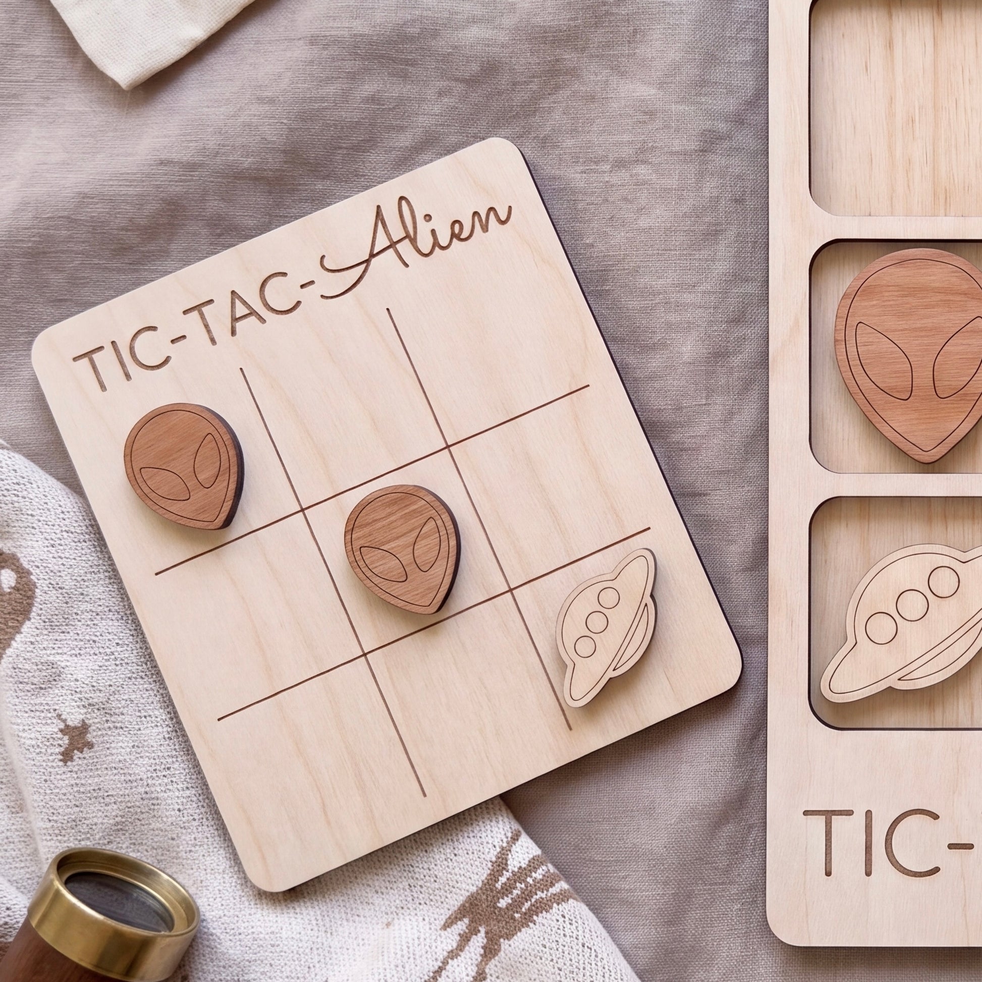 a wooden tic-tac game board with wooden alien and spaceship tiles, along with a wooden tic-tac game piece.