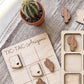 a wooden tic-tac game board labeled "TIC-TAC- Arizona" with wooden tiles shaped like cacti and a potted cactus plant.