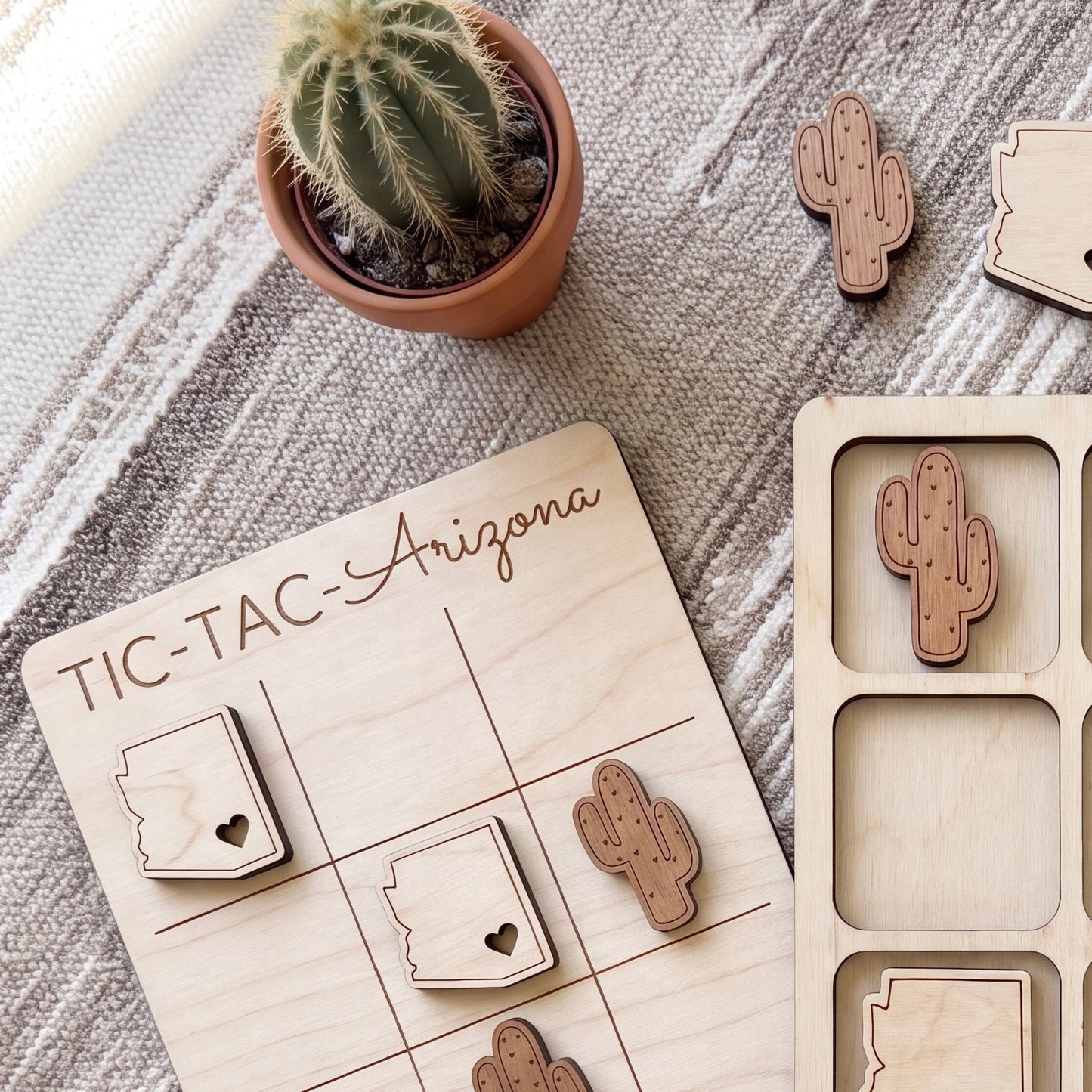 a wooden tic-tac game board labeled "TIC-TAC- Arizona" with wooden tiles shaped like cacti and a potted cactus plant.