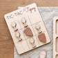 A wooden tic-tac game board with wooden pieces shaped like wine glasses and grapes, placed on a wooden surface.