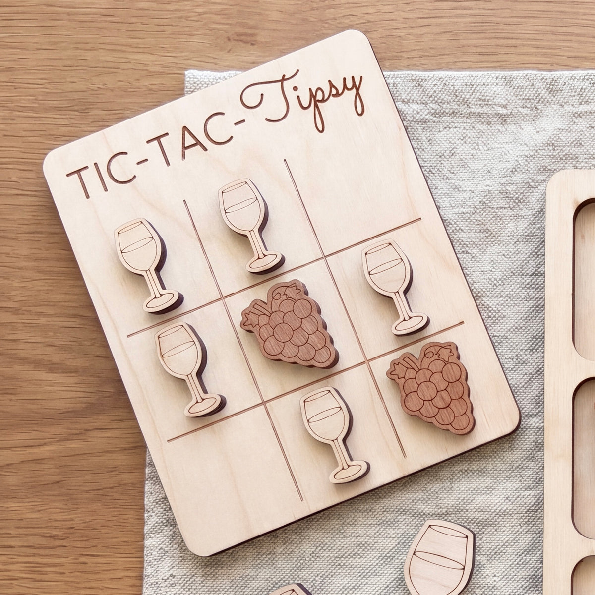 A wooden tic-tac game board with wooden pieces shaped like wine glasses and grapes, placed on a wooden surface.