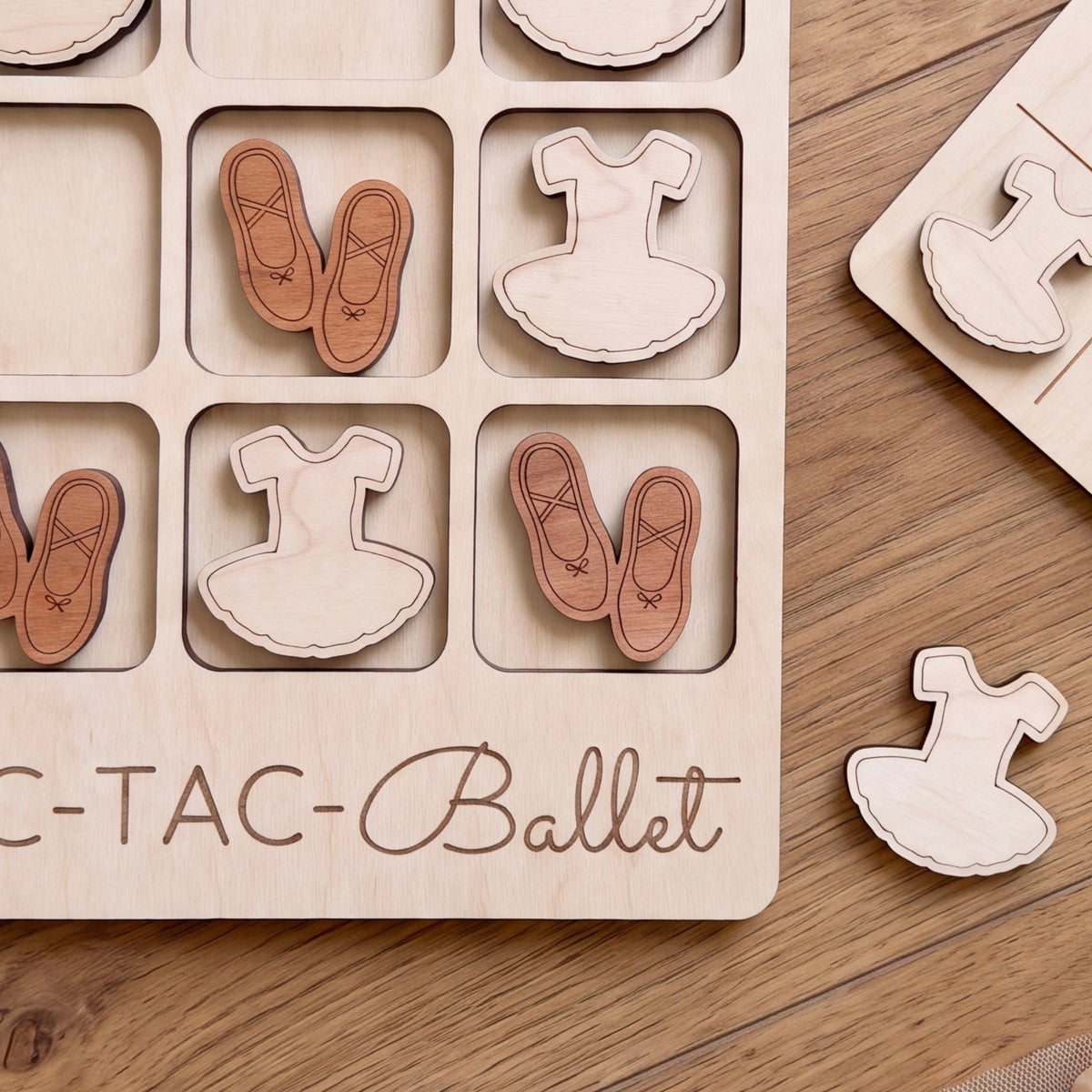 A wooden board game with a tic-tac-toe grid and wooden ballet tutus and ballet slippers as game pieces.