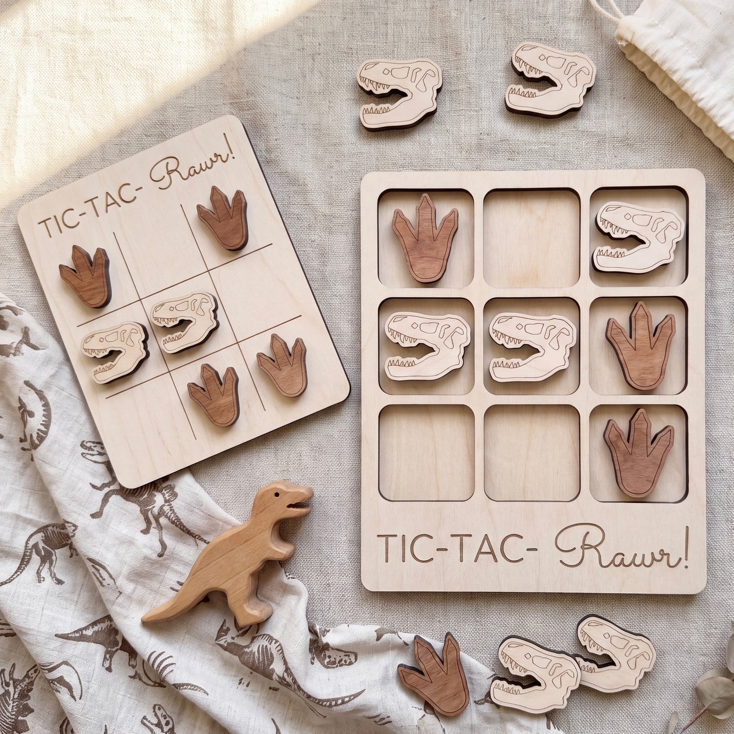 a wooden tic-tac game with dinosaur footprints and dinosaur toys, along with a wooden dinosaur toy.