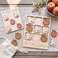 a wooden Tic-Tac game set with wooden pieces shaped like the states of Georgia, placed on a wooden surface alongside a bowl of peaches and a white cloth.