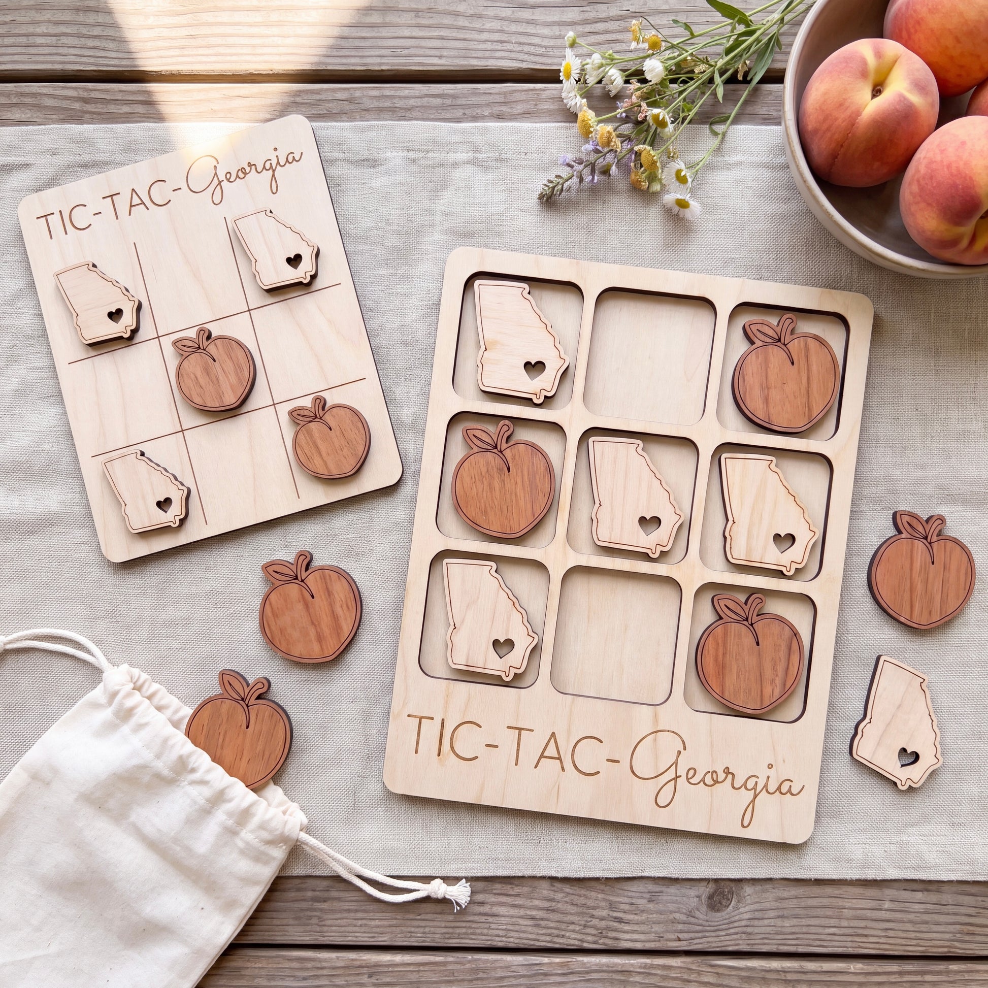 a wooden Tic-Tac game set with wooden pieces shaped like the states of Georgia, placed on a wooden surface alongside a bowl of peaches and a white cloth.