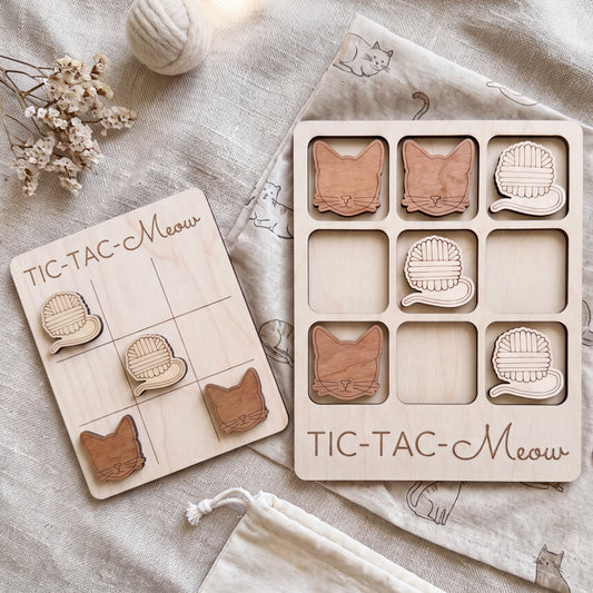 a wooden tic-tac game with cat-themed tiles and a wooden board with a cat-themed tile. There are also some cat-themed items, such as a ball and a bag, placed on a beige cloth.