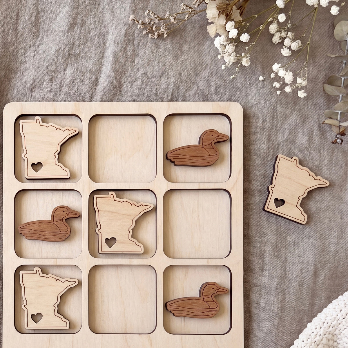 A wooden puzzle with nine pieces, each depicting a different state in Minnesota, including a Minnesota duck. The puzzle pieces are arranged in a 3x3 grid on a beige background.