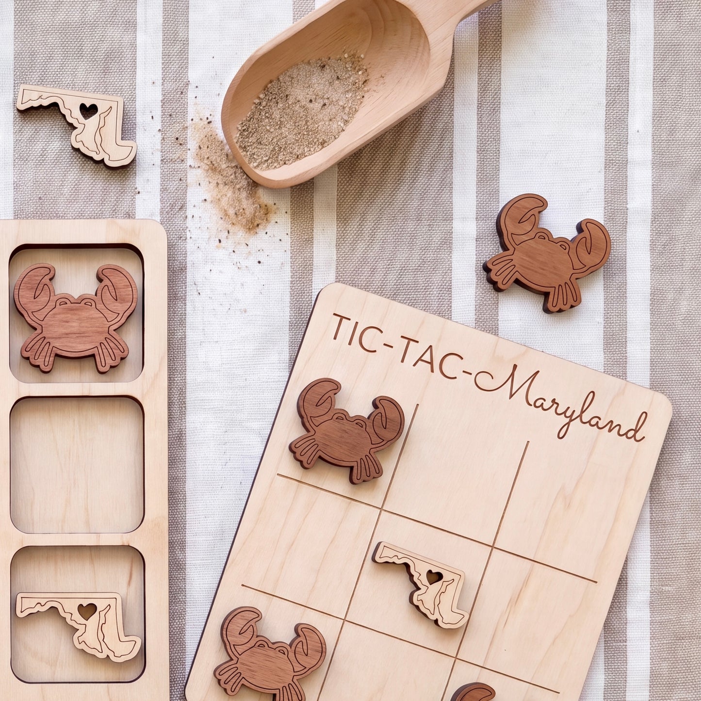a wooden tic-tac game board with a Maryland state on it, along with several wooden crab-shaped tiles and a wooden scoop.
