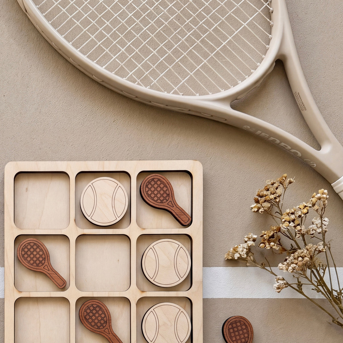 a wooden tic-tac-toe board with wooden tennis rackets and a bouquet of dried flowers on a beige surface.