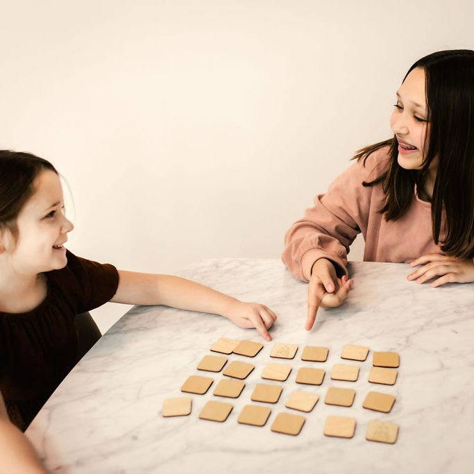 Two young girls are sitting at a marble table, engaged in a game with wooden blocks.