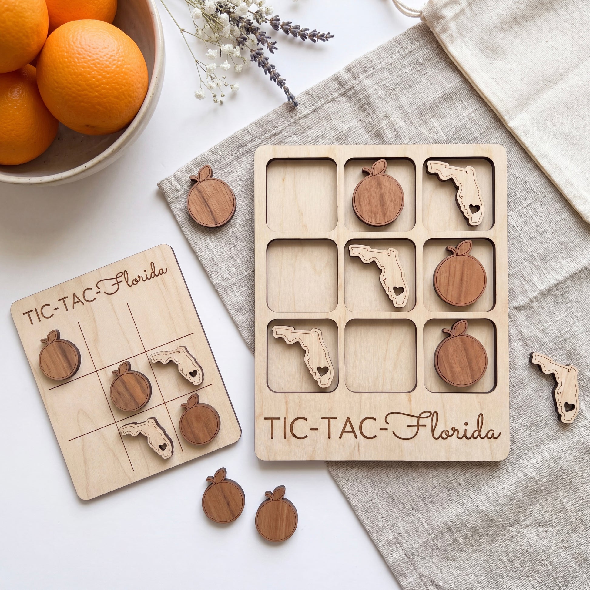 a wooden tic-tac game with Florida state shapes on it, along with a bowl of oranges and some flowers.