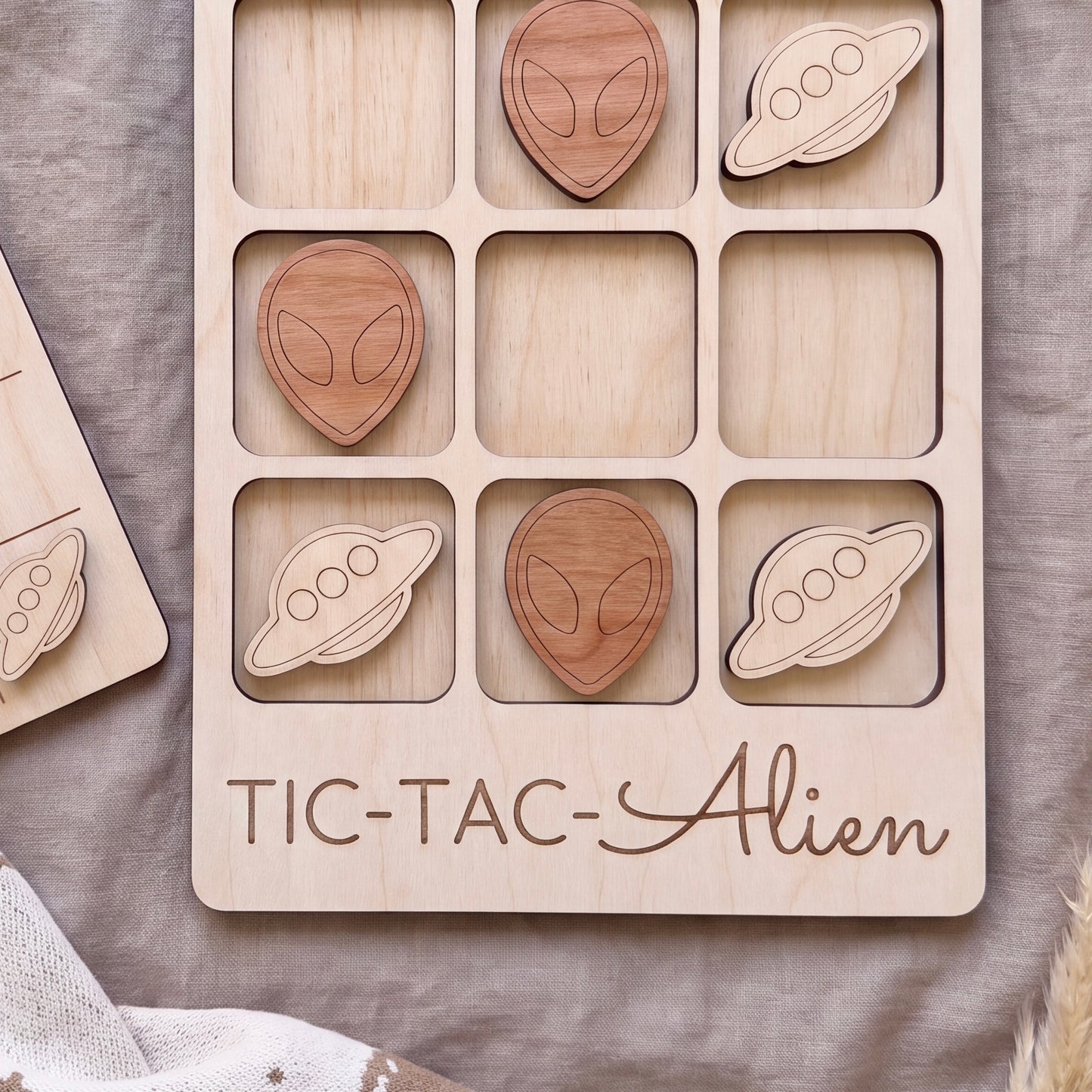 A wooden tic-tac game board with wooden alien and spaceship tiles, and the word "TIC-TAC-ALIEN" printed on it.