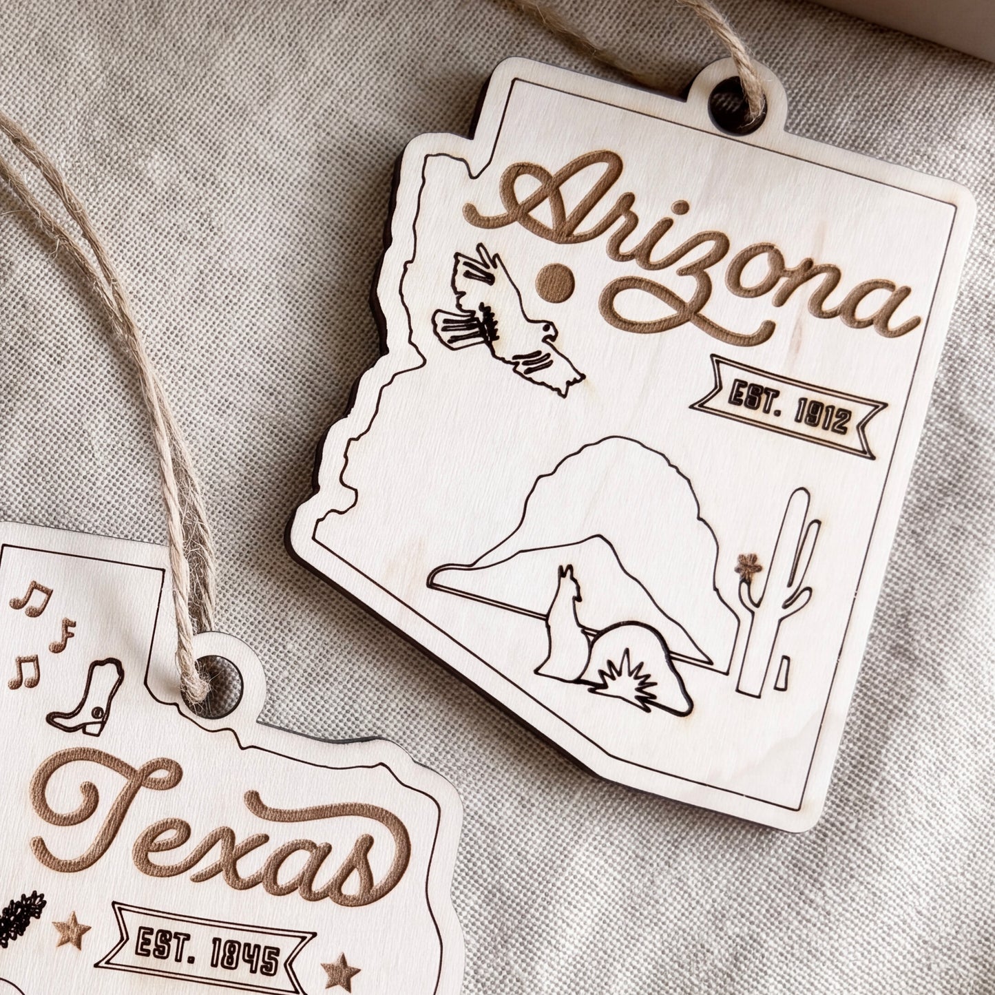 two wooden ornaments shaped like the state of Arizona, with various symbols and text related to the state.