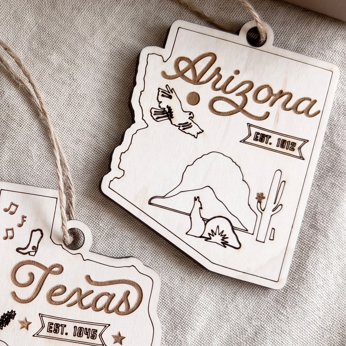 two wooden ornaments shaped like the state of Arizona, with various symbols and text related to the state.