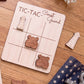 a wooden tic-tac game board with the words "TIC-TAC-Coast Guard" written on it, along with two wooden tic-tac pieces shaped like anchors. The game board is placed on a wooden surface, and there are some additional wooden objects, such as a star-patterned cloth and a small lighthouse-shaped object, in the background.
