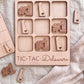 A wooden tic-tac game board with the word "TIC-TAC-Delaware" printed on it, along with several wooden pieces shaped like the state of Delaware.