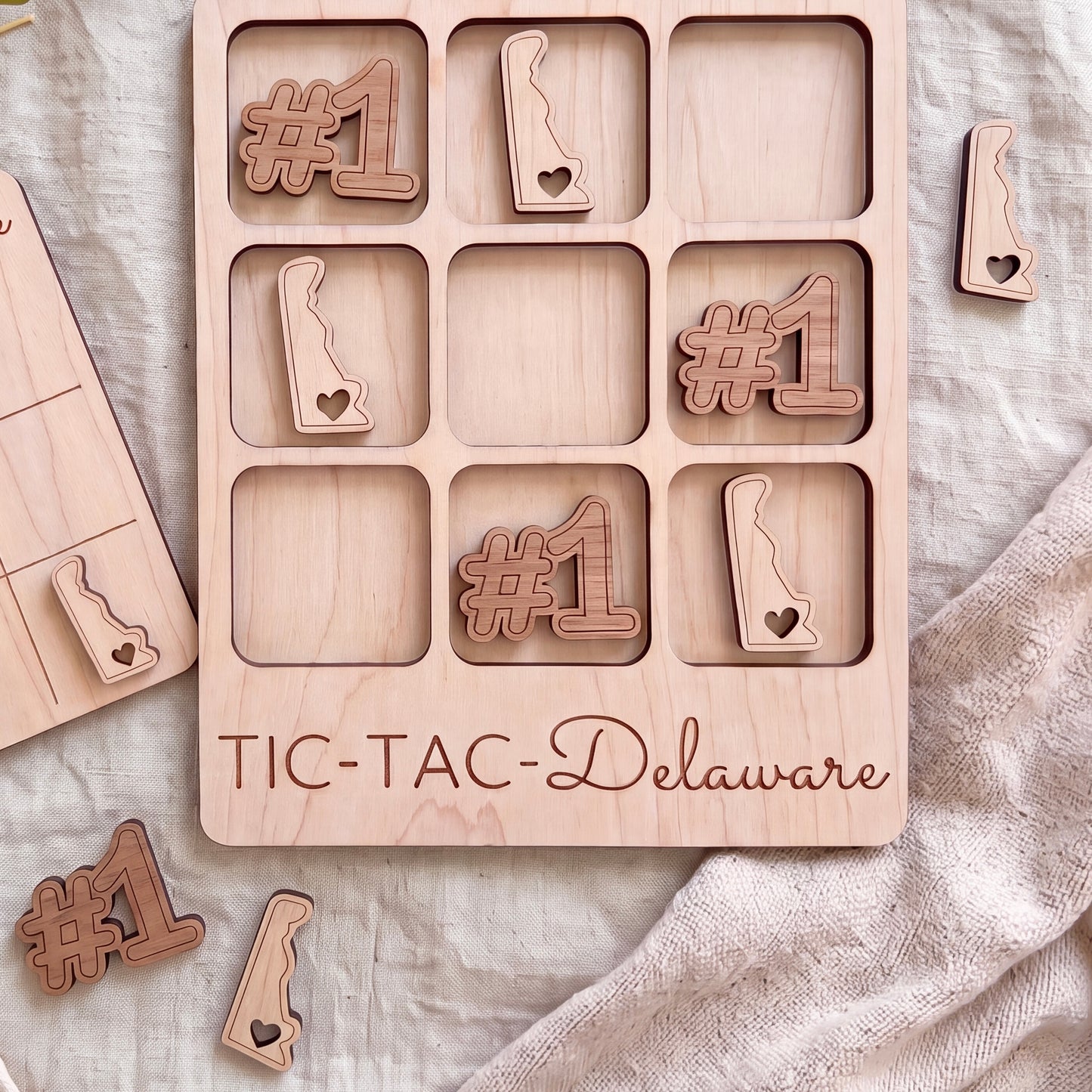 A wooden tic-tac game board with the word "TIC-TAC-Delaware" printed on it, along with several wooden pieces shaped like the state of Delaware.