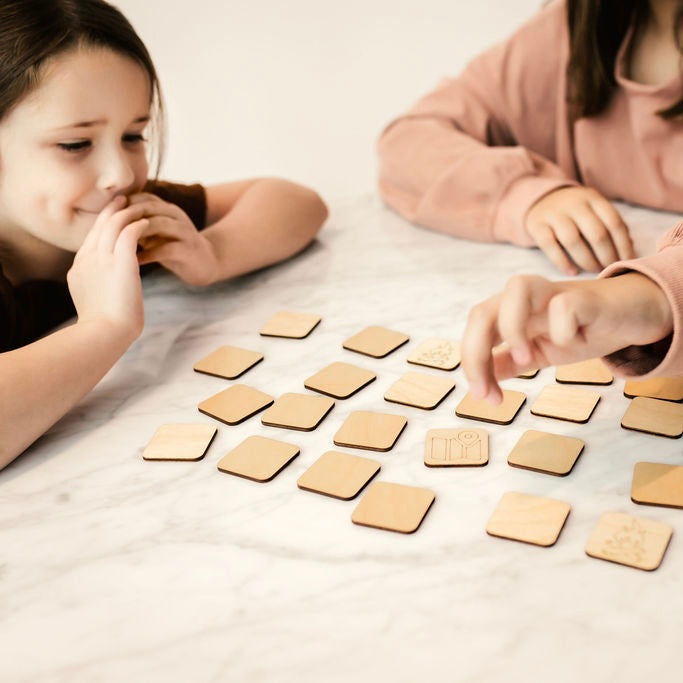 Two young girls are playing with wooden shapes on a marble countertop.